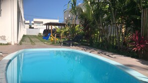 Una piscina con tobogán, rodeada de vegetación y un edificio moderno.