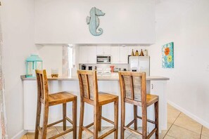 A kitchen with white cabinets, a microwave, and a seahorse decoration. There are three wooden chairs with woven seats. - Family Friendly Home with Private Pool and Dock on the Bay (Gulf Shores)