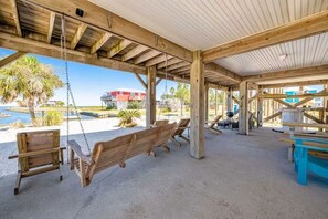 A covered outdoor area with wooden benches and tables, a swing, and a view of the beach and ocean. - Family Friendly Home with Private Pool and Dock on the Bay (Gulf Shores)