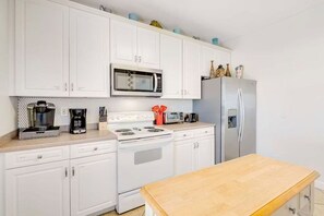 Eine Küche mit weißen Schränken, einer Mikrowelle, einem Herd, einem Kühlschrank und einem Holztisch.