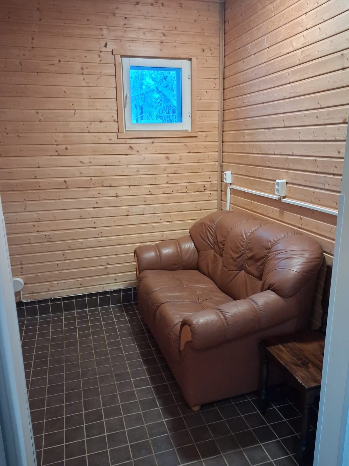 Pieni huone, jonka seinät ovat puuta, siinä on ruskea nahkasohva ja laattalattia.
