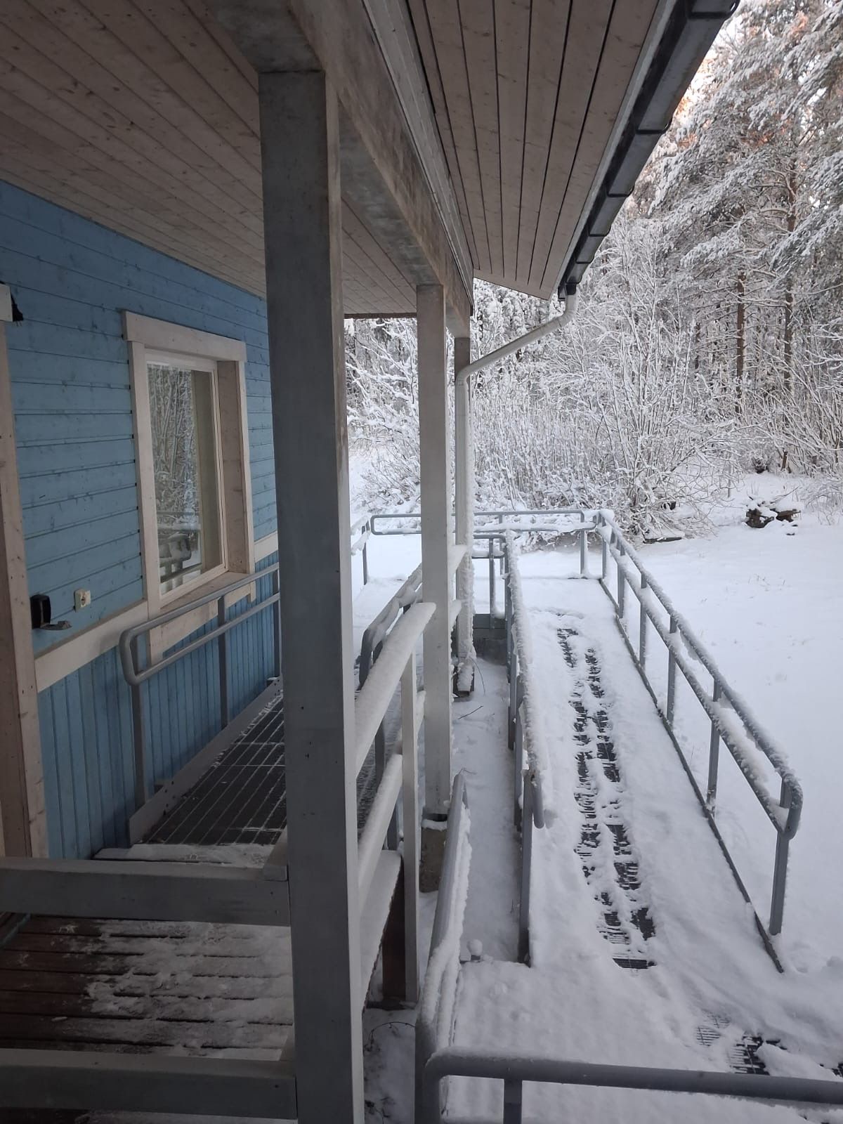 Ett takförsett utomhusområde med ett metallräcke, ett trädäck och en snötäckt mark.