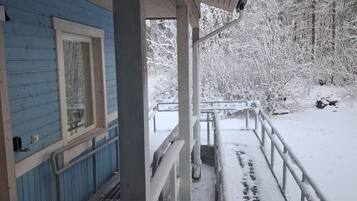 Ett takförsett utomhusområde med ett metallräcke, ett trädäck och en snötäckt mark.