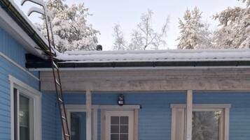 Een blauw gebouw met een witte deur en ramen, een metalen ladder die tegen de muur staat, en een met sneeuw bedekte grond.