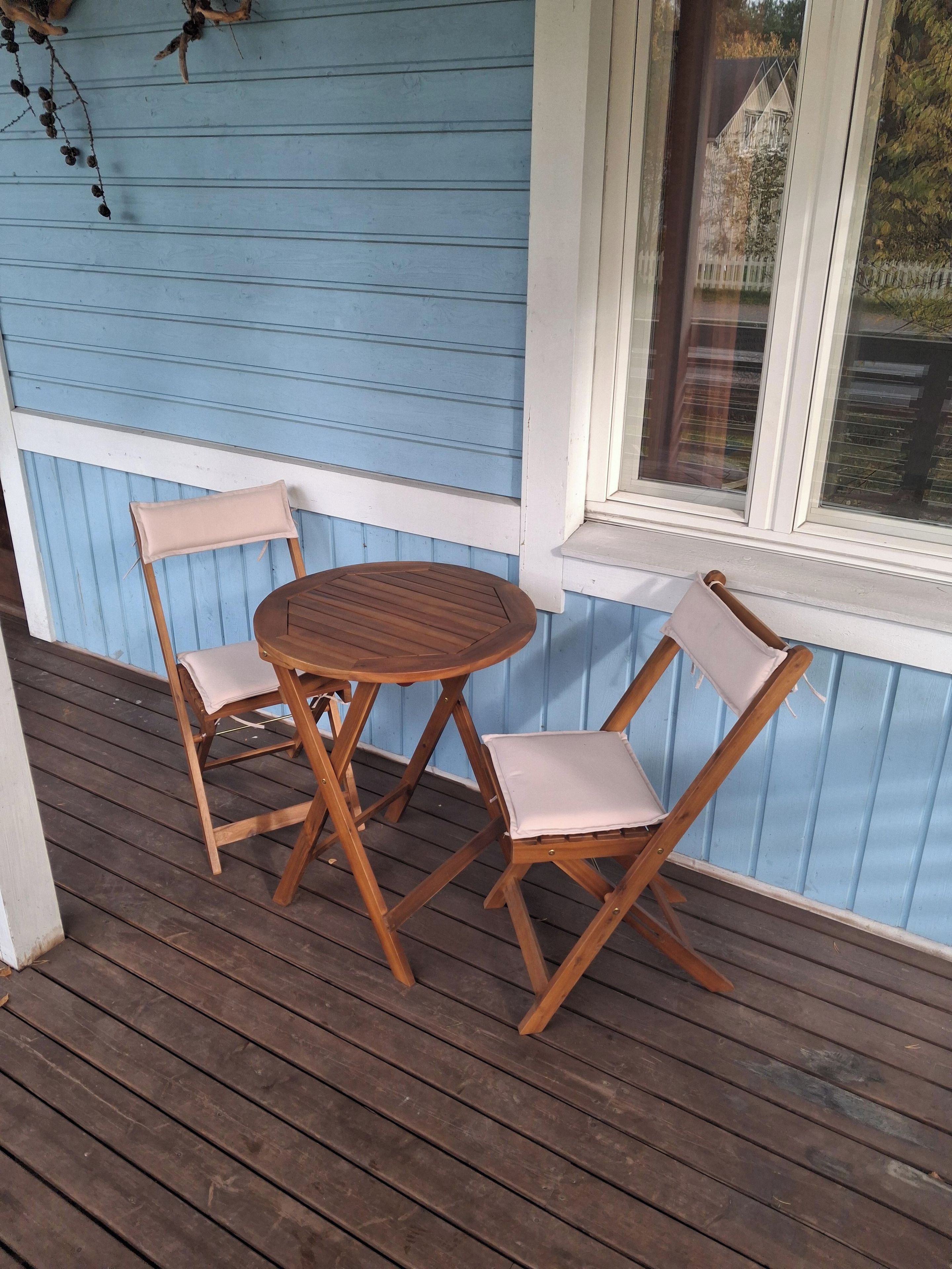 Een houten terras met een ronde tafel en twee stoelen.