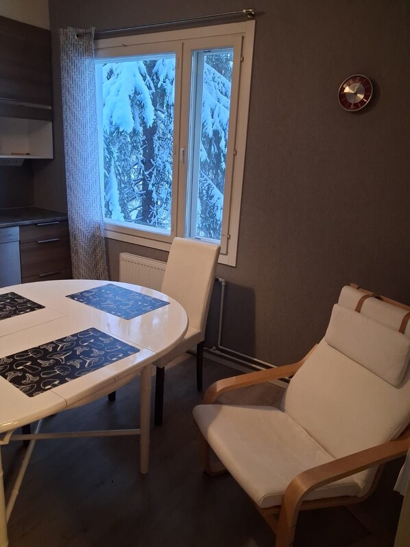 A room with a round table, a white chair, and a window with a view of snow-covered trees.