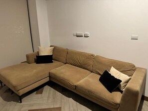 A tan sectional sofa with black cushions, a wooden floor, and a white wall with two light switches. - Aurea Luxury Apartment Z10 (Guatemala)