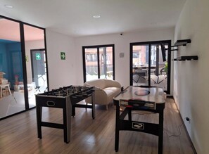 A room with two foosball tables, a sofa, and a view through glass doors. - Aurea Luxury Apartment Z10 (Guatemala)