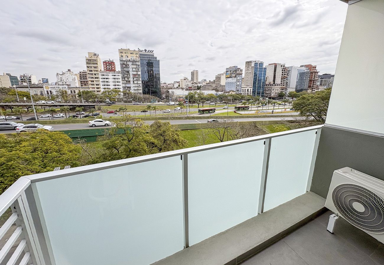 Ein Balkon mit Blick auf die Stadt, einem weißen Geländer und einem Standventilator.