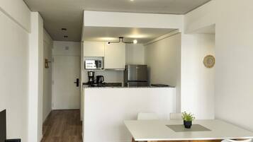 A modern kitchen with a refrigerator, microwave, and coffee maker. There is a dining area with a table and chairs.