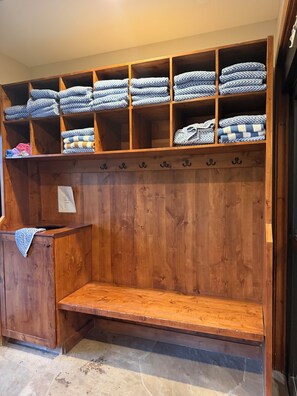 Un banco de madera con un estante superior que contiene toallas y mantas dobladas.