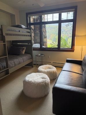 Una habitación con literas, un sofá, otomanas y una ventana con vistas a zonas verdes.