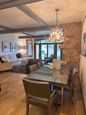A modern living room with a dining area, featuring a chandelier, stone wall, and large windows. - Snow Cloud Slope Side Dream
3 bedroom/3 1/2 bath ski in/ski out (Avon)