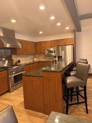 Una cocina moderna con armarios de madera, electrodomésticos de acero inoxidable, una isla central y un taburete de bar.