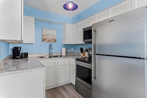 A modern kitchen with white cabinetry, a stainless steel refrigerator, a microwave, and a coffee maker. - Spanish Villas #58 - Block From The Beach (Indian Rocks Beach)