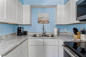 Una cocina moderna con armarios blancos, un lavamanos de acero inoxidable, una cafetera y una estufa.