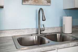 Una cocina con un lavamanos de acero inoxidable, un grifo y un rollo de toallas de papel en la encimera.