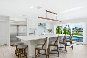A modern kitchen with a central island, bar stools, and a view of a swimming pool. - The Beach Life - 4 BR 2.5 BA  premier home w/ pool & waterview (Indian Rocks Beach)