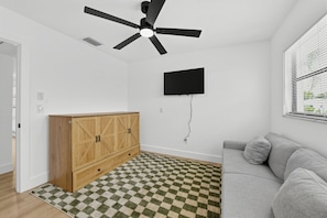 Ein Zimmer mit Deckenventilator, Wand-Fernseher, Holzschrank, kariertem Teppich und grauem Sofa.