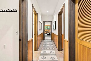A hallway with wooden doors, a patterned rug, and a view into a room with a window. - Sage Haven | Walk to Ski + Hot Tub & Deck (Ketchum)
