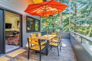 A wooden deck with a table and chairs, an umbrella, and a view of trees. - Sage Haven | Walk to Ski + Hot Tub & Deck (Ketchum)