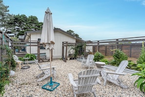 A patio with Adirondack chairs, a table, and a large umbrella. - Discover your new favorite hideaway, Casitas By The Sea (Fort Bragg)
