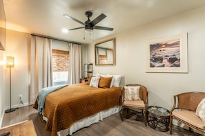 A bedroom with a bed, a ceiling fan, a bedside table, a chair, a small table, and a framed picture on the wall. - Discover your new favorite hideaway, Casitas By The Sea (Fort Bragg)