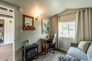 A cozy room with a wooden desk, a chair, a sofa, a fireplace, and a window with curtains. - Discover your new favorite hideaway, Casitas By The Sea (Fort Bragg)