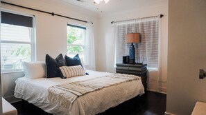 Ein Schlafzimmer mit einem Bett, Kissen, einer Nachttischlampe und einem Fenster mit Vorhängen.