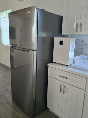 A stainless steel refrigerator and a white mini-fridge in a kitchen with white cabinets and a tiled backsplash. - Emerald Escape - brand new 2-bedroom house on private beachfront property (Russell Island)