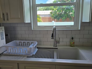A kitchen with a stainless steel sink, a window, and a white tiled backsplash. - Emerald Escape - brand new 2-bedroom house on private beachfront property (Russell Island)
