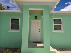 A house with a green exterior, a white door, and two windows with white frames. - Emerald Escape - brand new 2-bedroom house on private beachfront property (Russell Island)