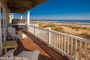 Eine Holzterrasse mit Sitzgelegenheit, einem Fernseher und Blick auf Strand und Meer.