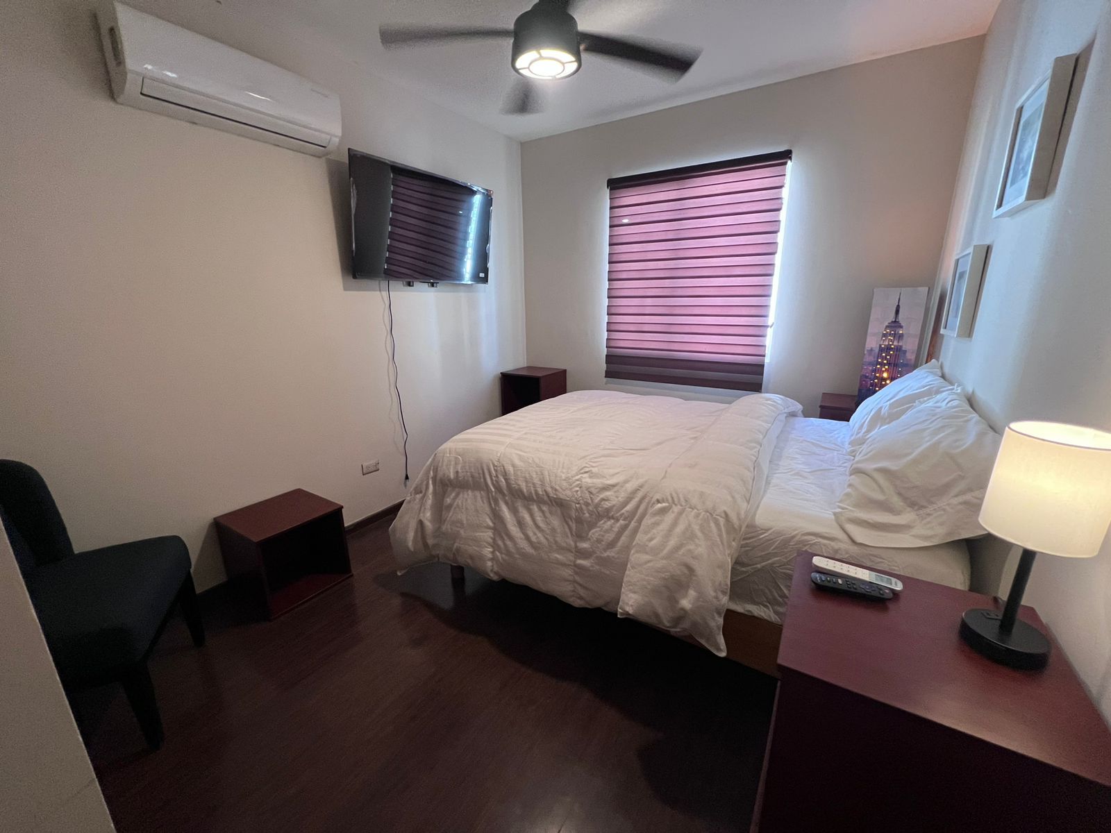 Una habitación de hotel con cama, mesita de noche, lámpara y ventilador de techo.