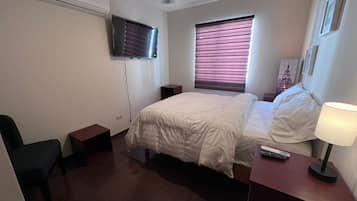 Una habitación de hotel con cama, mesita de noche, lámpara y ventilador de techo.