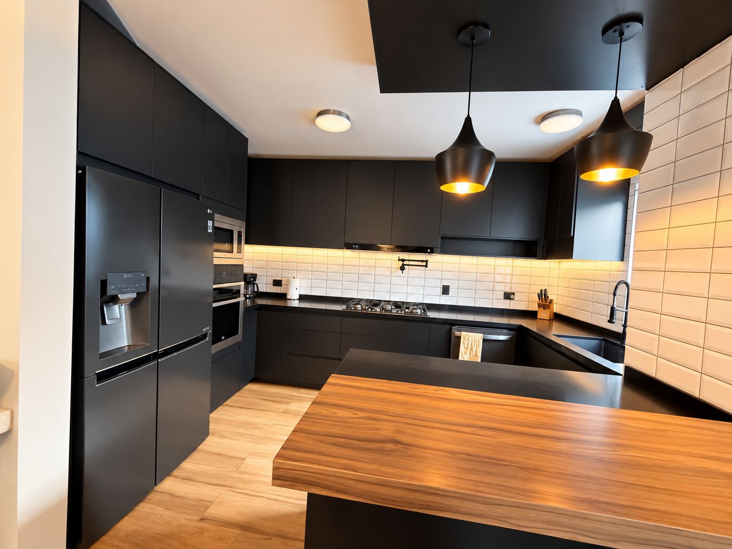 A modern kitchen with dark cabinetry, a wooden countertop, and pendant lighting.