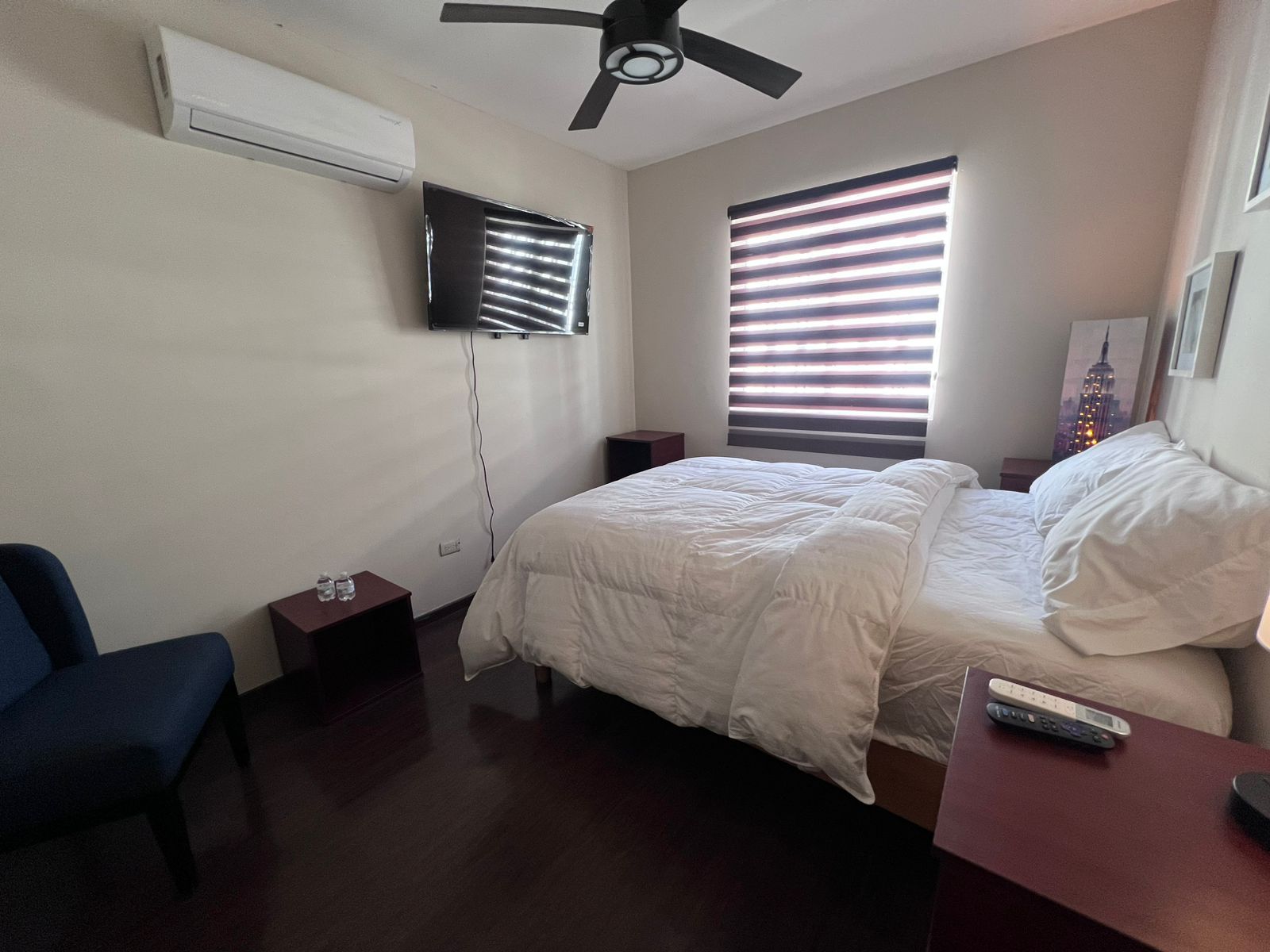 Een slaapkamer met een bed, een stoel, een aan de muur bevestigde televisie en een plafondventilator.