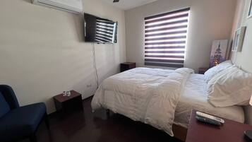 Een slaapkamer met een bed, een stoel, een aan de muur bevestigde televisie en een plafondventilator.