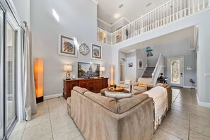 A spacious living room with a high ceiling, a staircase, and a view of a castle. - Modern Kissimmee 5 Bedroom Home, Orlando Villa 6674 (Orlando)