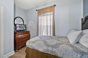 Ein Schlafzimmer mit einem Bett, einer Kommode, einem Fernseher und einem Fenster mit Vorhängen.
