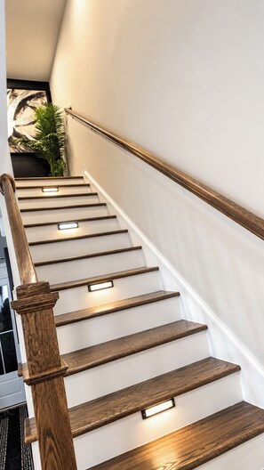 Una escalera con escalones y barandilla de madera, iluminada por luces debajo de la escalera.