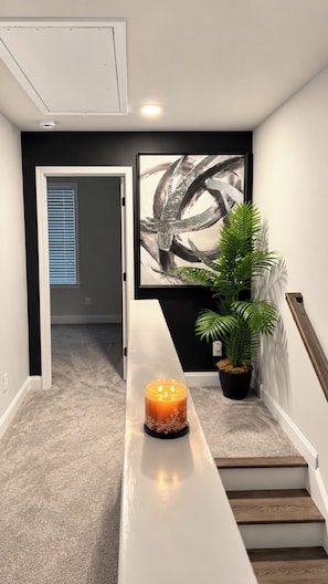 A hallway with a white bench, a lit candle, a framed abstract painting, and a potted plant. -     Luxury 2BR Summerville Retreat / Modern, Cozy & Close to Everything (Summerville)