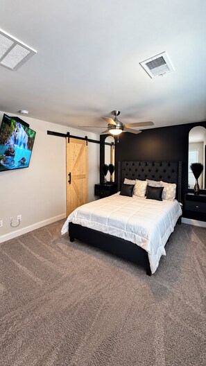 A bedroom with a bed, a ceiling fan, a mounted TV, and a wooden door. -     Luxury 2BR Summerville Retreat / Modern, Cozy & Close to Everything (Summerville)