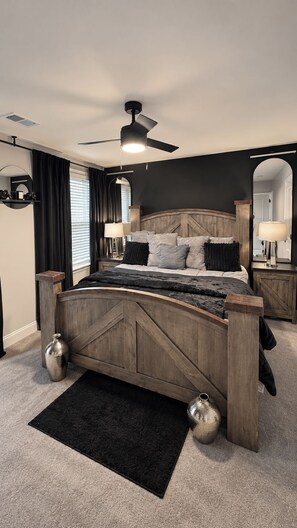Un dormitorio con cama de madera, ventilador de techo, alfombra negra y un espejo grande.