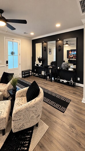 A living room with a black and white color scheme, a ceiling fan, and a television. -     Luxury 2BR Summerville Retreat / Modern, Cozy & Close to Everything (Summerville)