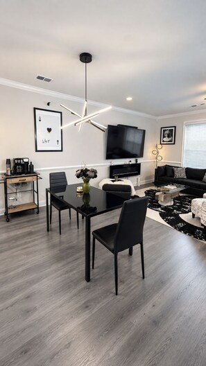 A modern living room with a dining area, a flat-screen TV mounted on the wall, and a black sofa. -     Luxury 2BR Summerville Retreat / Modern, Cozy & Close to Everything (Summerville)