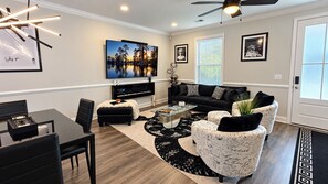 A modern living room with a black and white patterned sofa, a glass coffee table, and a large painting of a sunset over water. -     Luxury 2BR Summerville Retreat / Modern, Cozy & Close to Everything (Summerville)