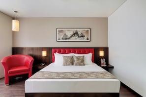 A hotel room with a red upholstered chair, a large bed with white linens, a red tufted headboard, and a framed picture on the wall. - (Hubli)