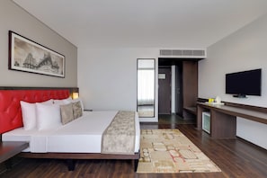 A hotel room with a red upholstered headboard, a large bed, a flat-screen TV, a small desk, and a large framed picture on the wall. - (Hubli)