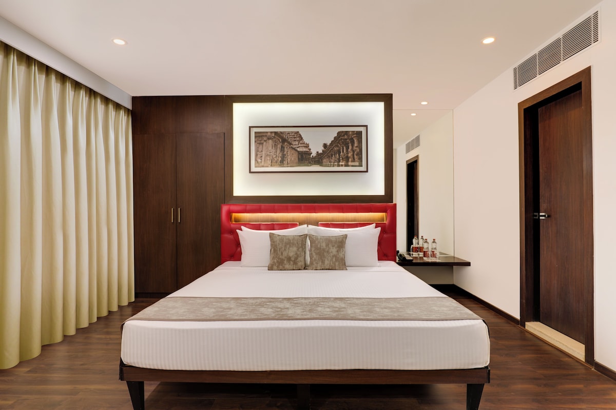Een moderne hotelkamer met een groot bed, een rood hoofdeinde, een ingelijste foto boven het bed en een houten garderobe.